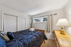 A bedroom with a bed, a nightstand, a lamp, and a window with curtains. - Your Tahoe Adventure Basecamp Near Heavenly — Midweek Discounts (South Lake Tahoe)