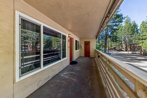 A covered corridor with large windows, a red door, and a wooden railing overlooking a parking area. - Your Tahoe Adventure Basecamp Near Heavenly — Midweek Discounts (South Lake Tahoe)