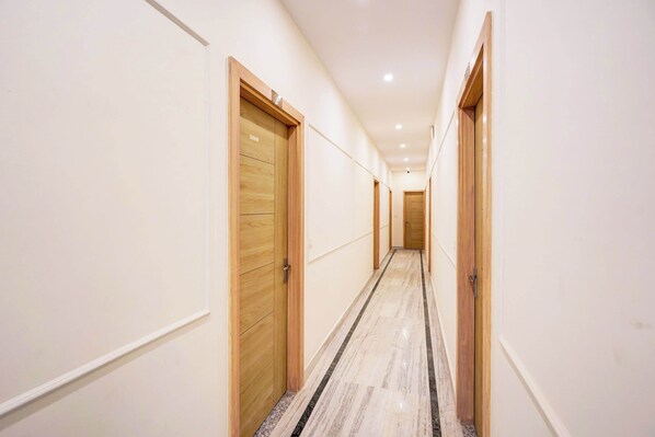 A corridor with wooden doors, white walls, and a marble floor. - Super Collection O Surajpur Chowk (Greater Noida)