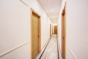 A corridor with wooden doors, white walls, and a marble floor. - Super Collection O Surajpur Chowk (Greater Noida)