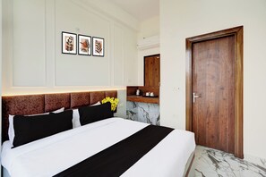 A hotel room with a bed, a wooden door, a marble floor, and a wall-mounted shelf with a mirror. - Super Collection O Surajpur Chowk (Greater Noida)