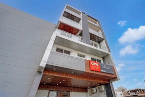 A multi-story building with a prominent vertical design element, a signboard for 'OYO Book on the App', and a wooden facade. - Super Collection O Surajpur Chowk (Greater Noida)