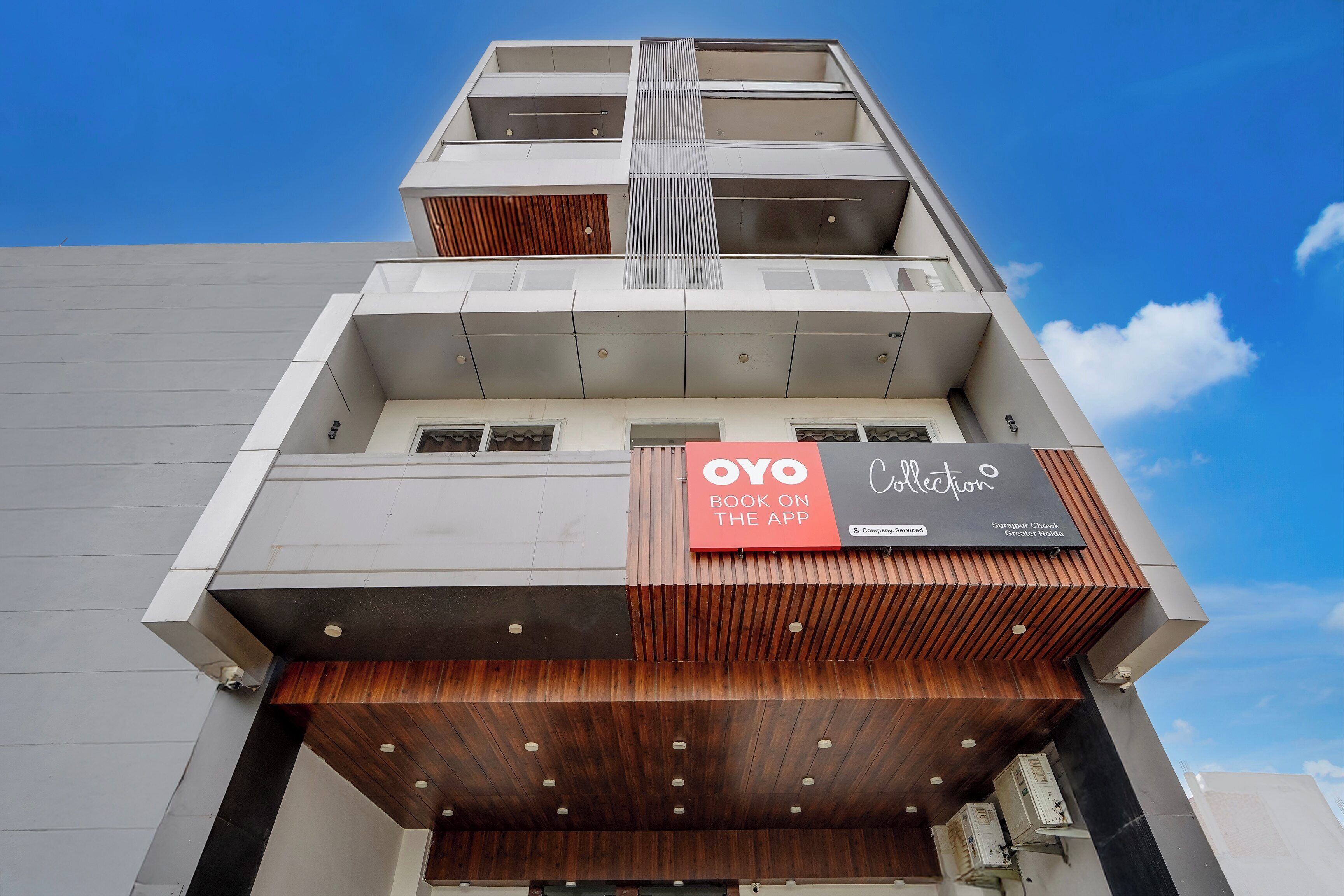 A modern building with a prominent OYO Collection sign, indicating a booking option via app.