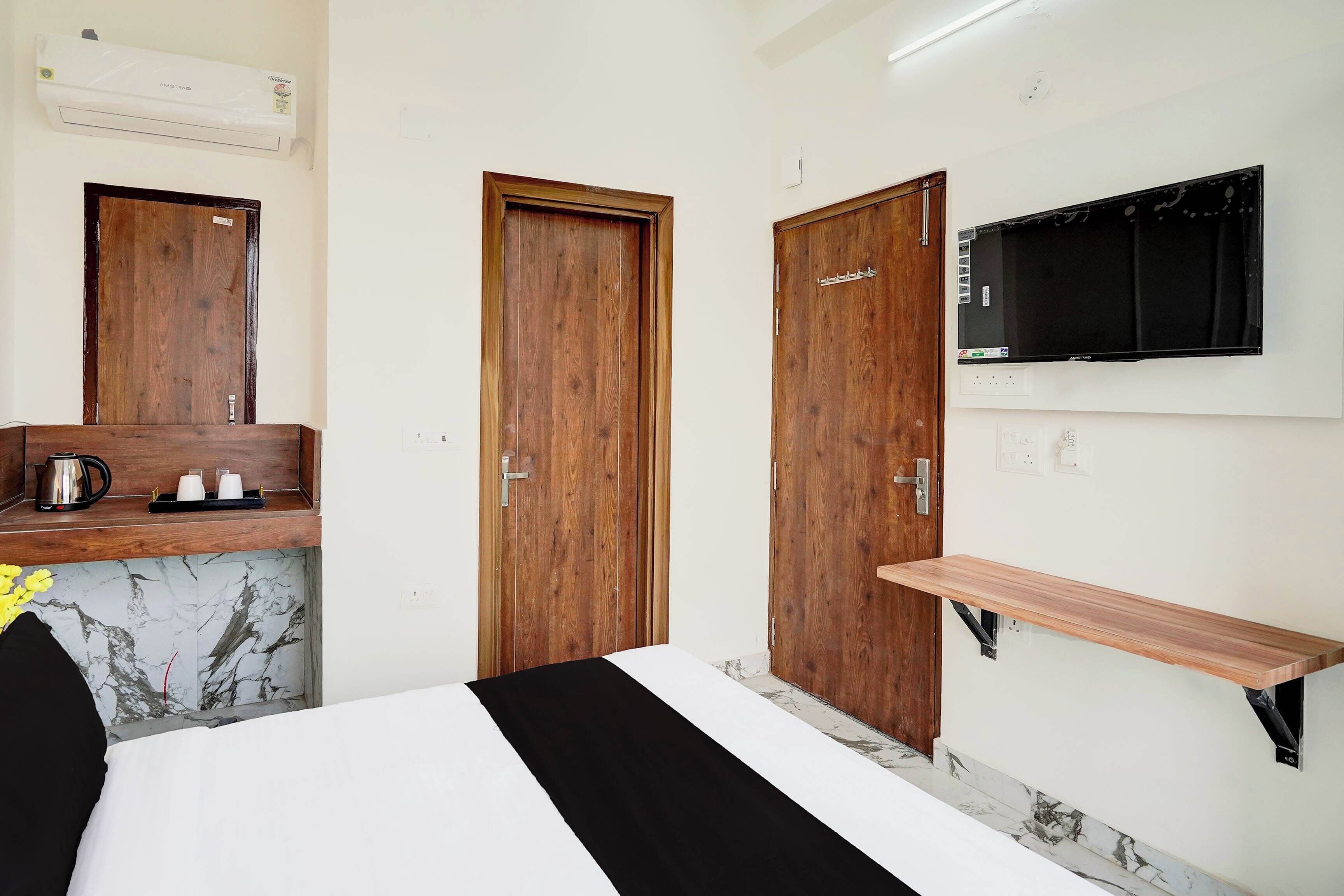 A hotel room with a bed, a wooden wardrobe, a television mounted on the wall, and a marble-patterned wall.