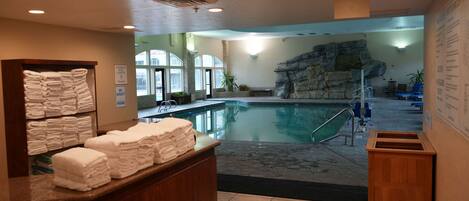 A pool area with a spa capacity sign, a stack of towels, and a reception desk.