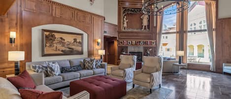 A spacious living room with a fireplace, wooden paneling, and a large chandelier.