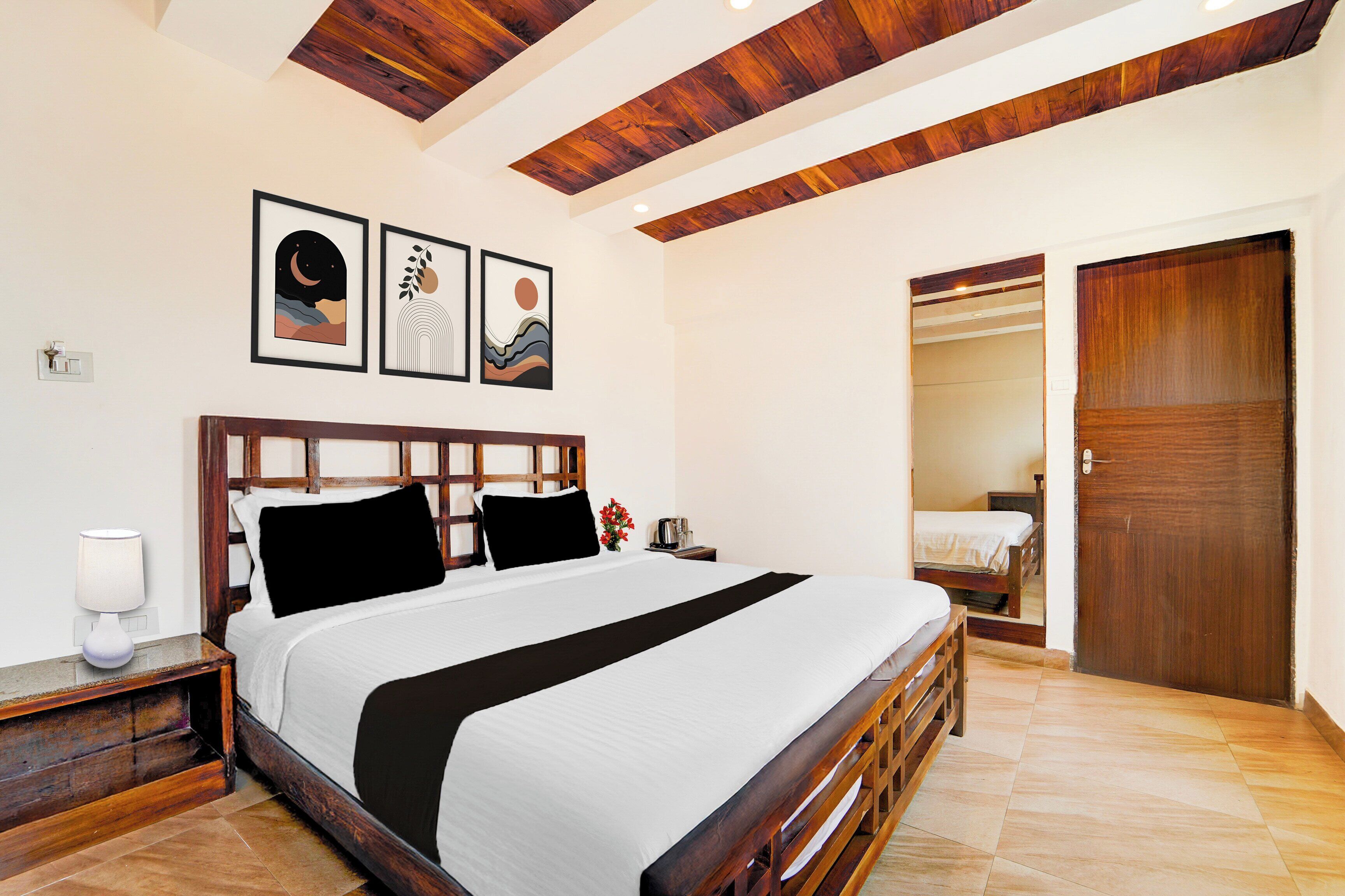 A bedroom with a wooden bed frame, a nightstand, a bedside table, and a wall-mounted light. There is a door leading to another room.