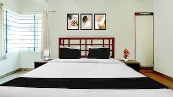 A hotel room with a large bed, a nightstand with a lamp, a window with curtains, and three framed artworks on the wall.