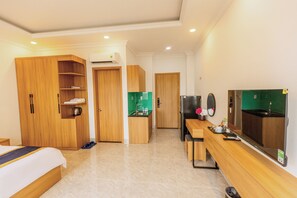 A hotel room with a bed, a wooden wardrobe, a kitchenette, and a large mirror.