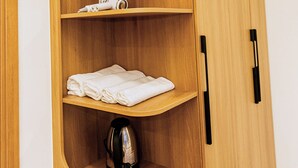 A wooden cabinet with three shelves, one of which holds a kettle and towels.