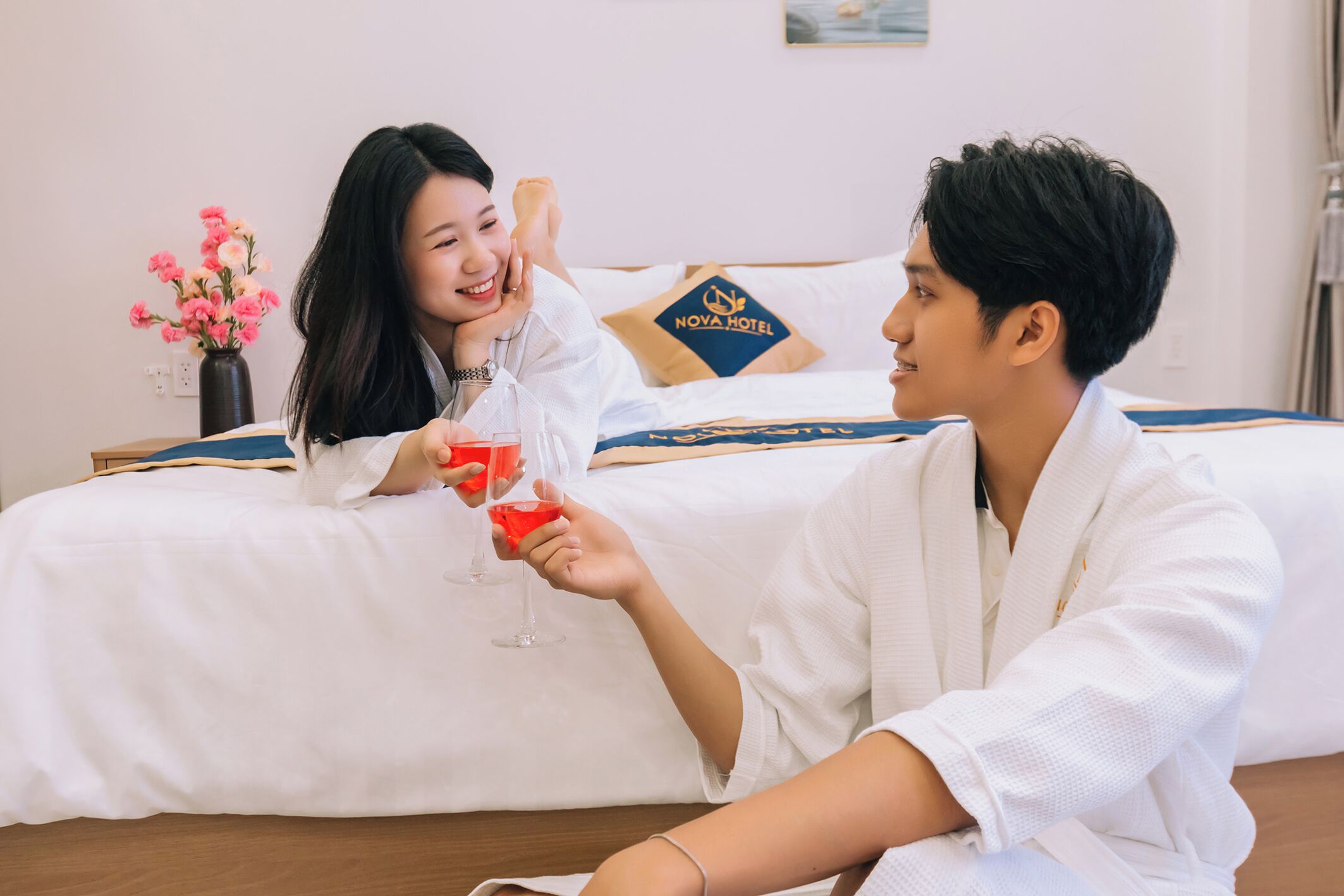 Una habitación de hotel con una cama, un florero de flores y una almohada con el logotipo del hotel.