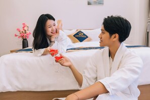 A hotel room with a bed, a vase of flowers, and a pillow with the hotel's logo.