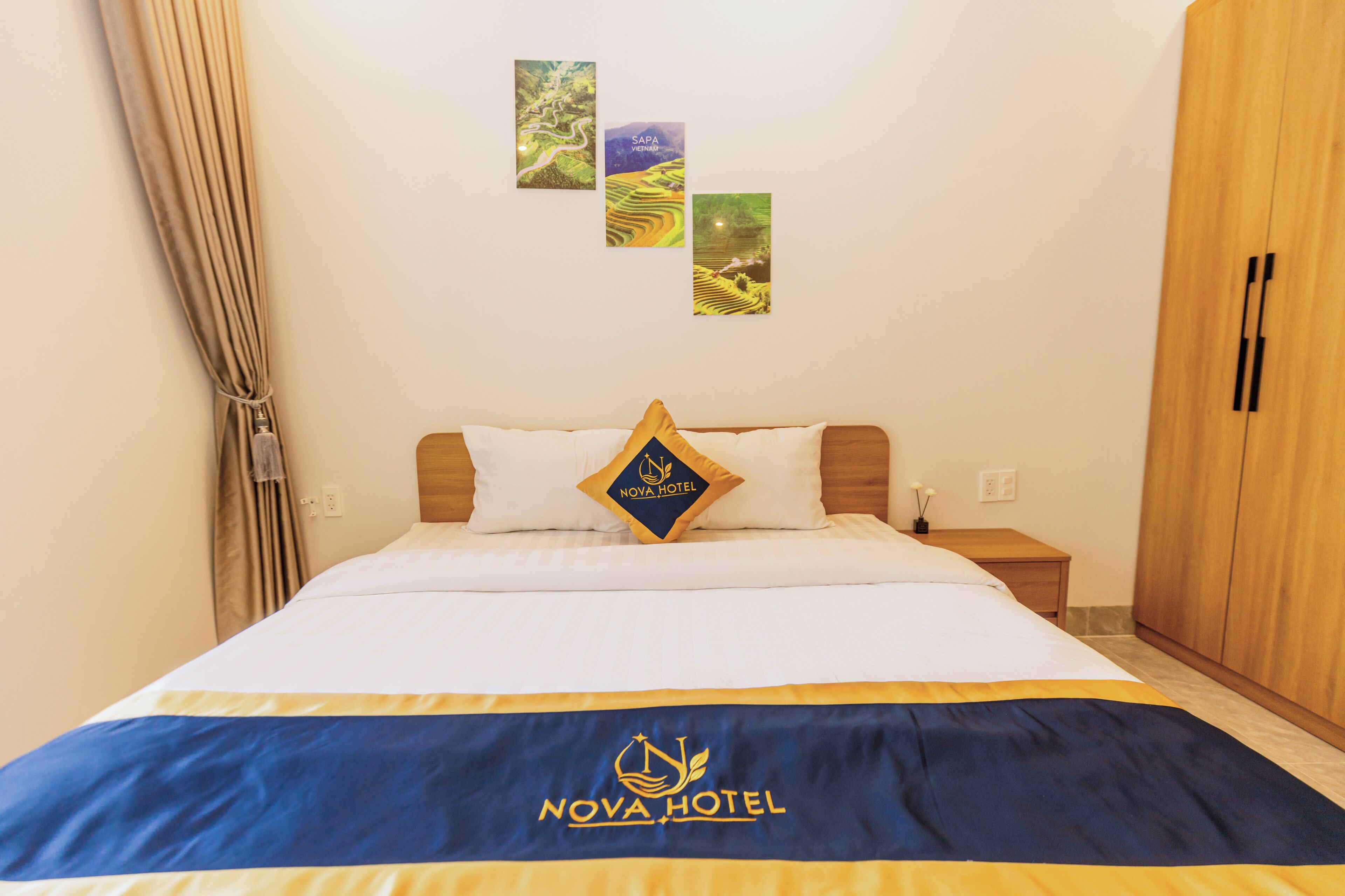 A hotel room with a bed, a nightstand, a wardrobe, and wall art depicting landscapes.
