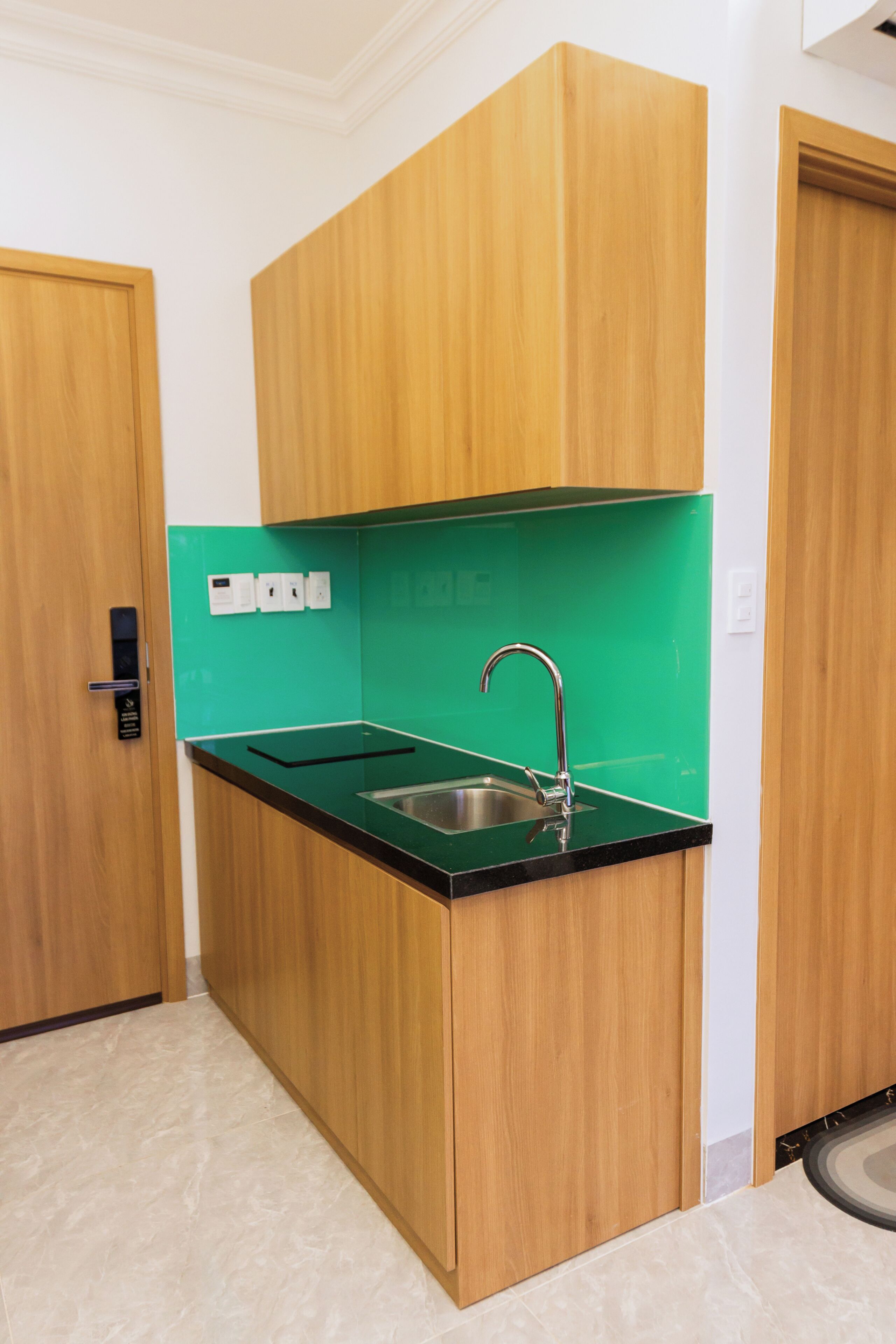 Una cocina compacta con armarios de madera, una encimera negra y un lavamanos de acero inoxidable.