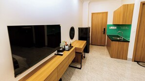A compact hotel room with a bed, a TV, a small kitchenette, and a wooden vanity.
