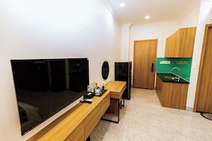 A compact hotel room with a bed, a TV, a small kitchenette, and a wooden vanity.