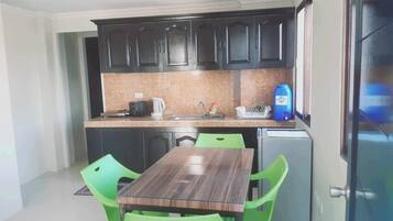 Una cocina compacta con armarios oscuros, una encimera, un lavabo, una cocina y una pequeña nevera, además de una mesa de comedor con sillas verdes.