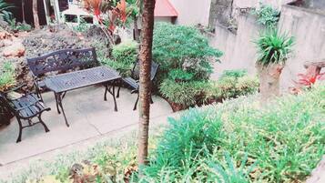 An outdoor seating area with a table and benches, surrounded by various plants and trees.