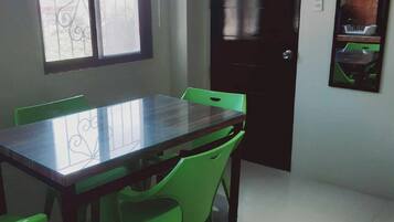 A dining area with a glass-top table and green chairs, a window with a metal railing, and a dark door.