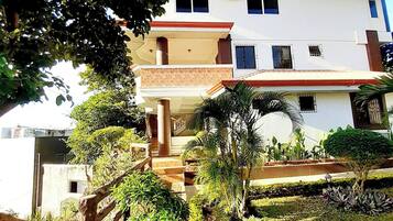 A multi-story building with a red roof, surrounded by lush greenery and a wooden fence.