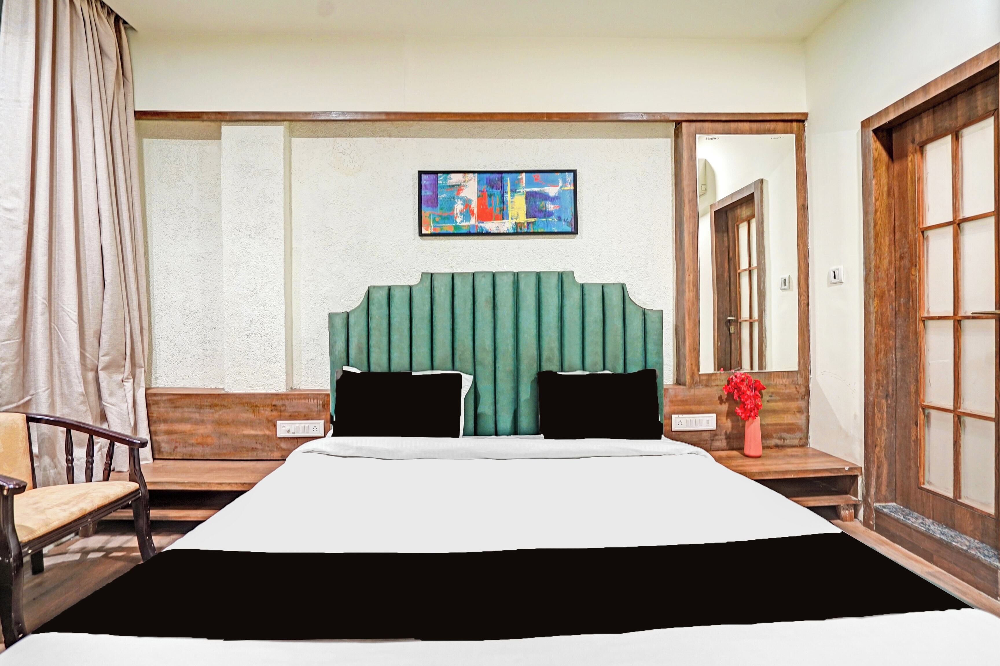 Habitación de hotel con una cama grande, cabecera verde, un cuadro en la pared y una puerta de madera.