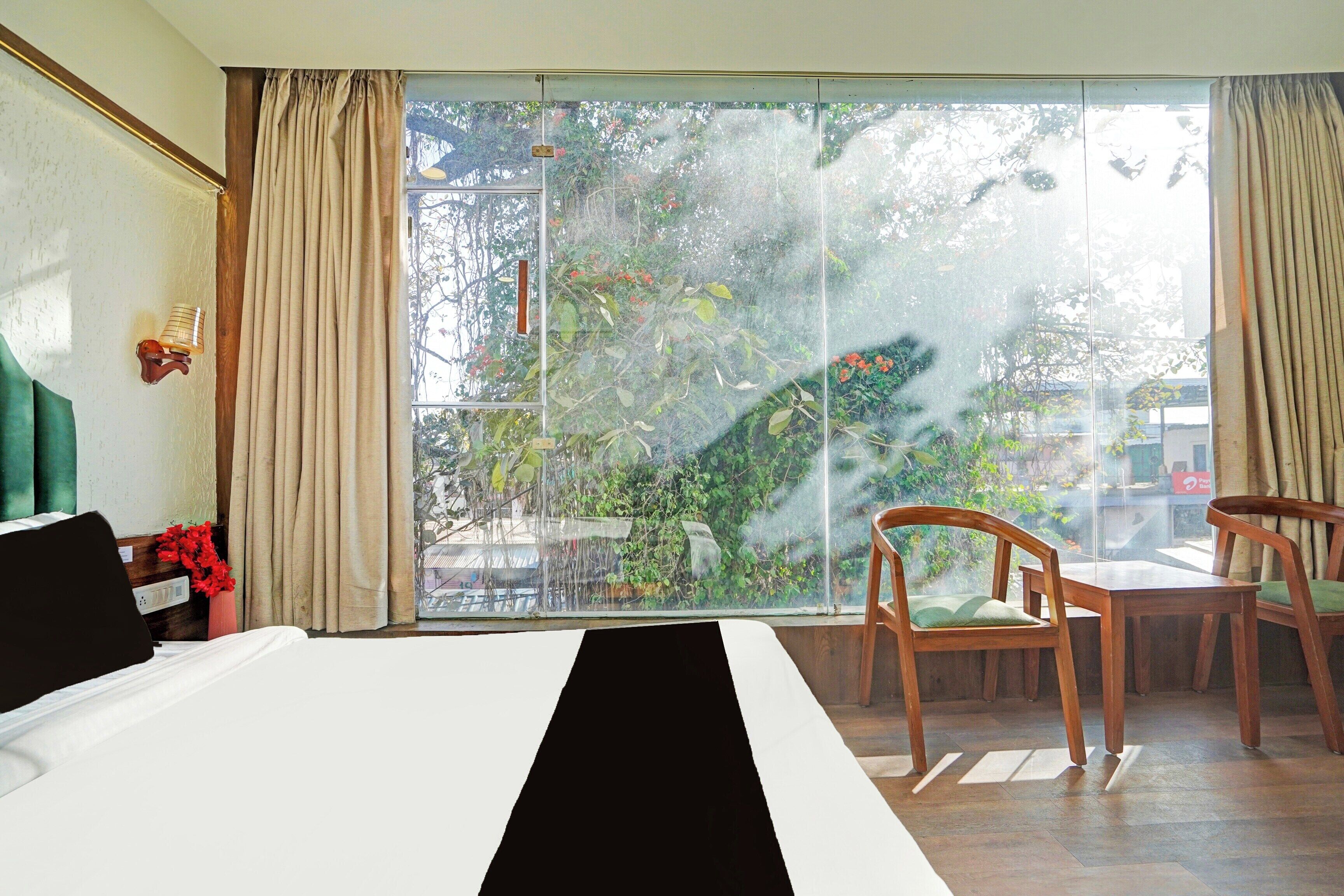 A hotel room with a large window, a bed, a chair, and a small table.