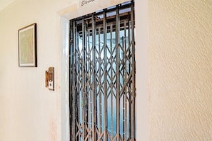 A door with a metal security gate, a wall-mounted light switch, and a framed picture. - Collection O Arvind Marg Pachamarhi (Pachmarhi)