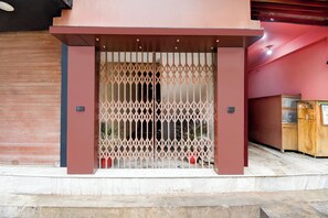 A modern building entrance with a metal gate, a closed shutter on the left, and a wooden cabinet on the right.