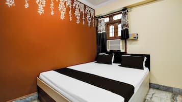 Una habitación de hotel con cama, ventana con cortinas, equipo de aire acondicionado y una pared con estampado floral.