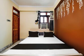 A hotel room with a bed, a window with curtains, a wall-mounted air conditioning unit, and a door.