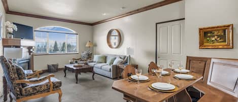A dining area with a wooden table set for four, a sofa, and a television in the background.