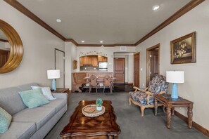 A living room with a sofa, a coffee table, and a floral armchair. There is a dining area with a table and chairs, and a kitchen in the background. - Zermatt Mountain Suite and 1bdr (Midway)
