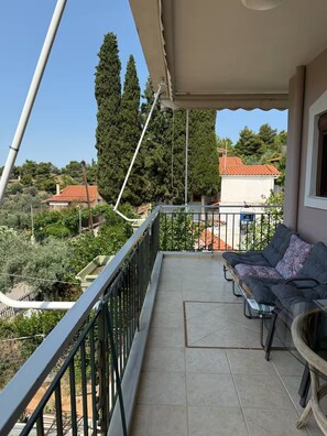 A balcony with a sofa and a table, overlooking a residential area with trees and houses. - Eretria Panorama Seaview Retreat with Balcony (malakonta)