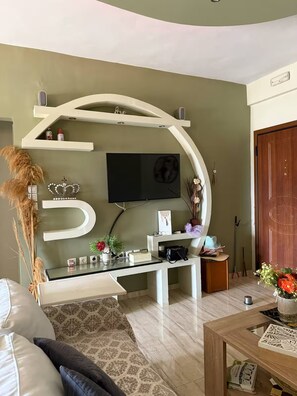 Un salon au design moderne, comprenant un grand chiffre « 5 » décoratif sur le mur, un téléviseur à écran plat et une table basse sur laquelle est posé un vase de fleurs.