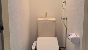 Casa de banho pequena e compacta, com sanita, secador de mãos e dispensador de toalhas de papel.