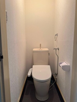 A small, compact bathroom with a toilet, a hand dryer, and a paper towel dispenser. - Spacious 4-Bedroom, 2-Bathroom House Near Kyoto: Nintendo Museum & Torii Gates (Uji)