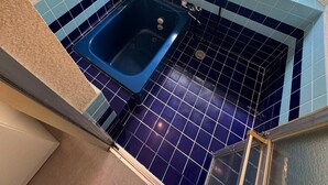 Um banheiro pequeno com uma banheira azul, uma janela e piso ladrilhado.