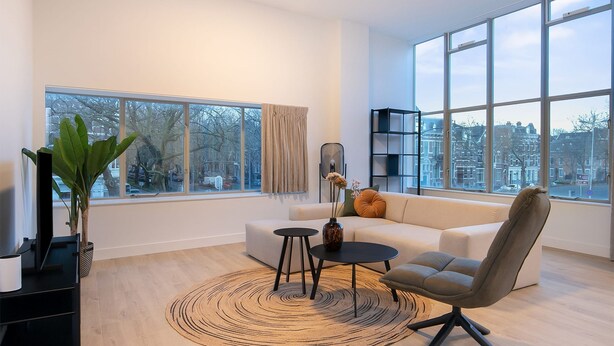 A modern living room with a large window, a sofa, a chair, a small table, and a plant. - Modern 2 Bedroom Apartment in Rotterdam City Center With Free Parking (Rotterdam)