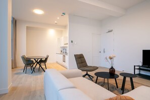 A modern living room with a sofa, a dining table with chairs, a coffee table, a TV, and a small side table with a vase. - Modern 2 Bedroom Apartment in Rotterdam City Center With Free Parking (Rotterdam)