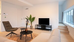 Ein modernes Wohnzimmer mit einer Couch, einem Sessel, einem Couchtisch, einem Fernseher und einer Pflanze.