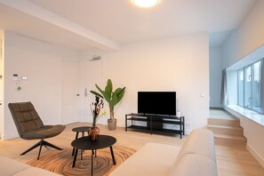 Ett modernt vardagsrum med en soffa, en fåtölj, ett soffbord, en tv och en växt.