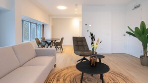Ein modernes Wohnzimmer mit einer Couch, einem Esstisch mit Stühlen, einem Couchtisch mit einer Vase und einem großen Fenster.