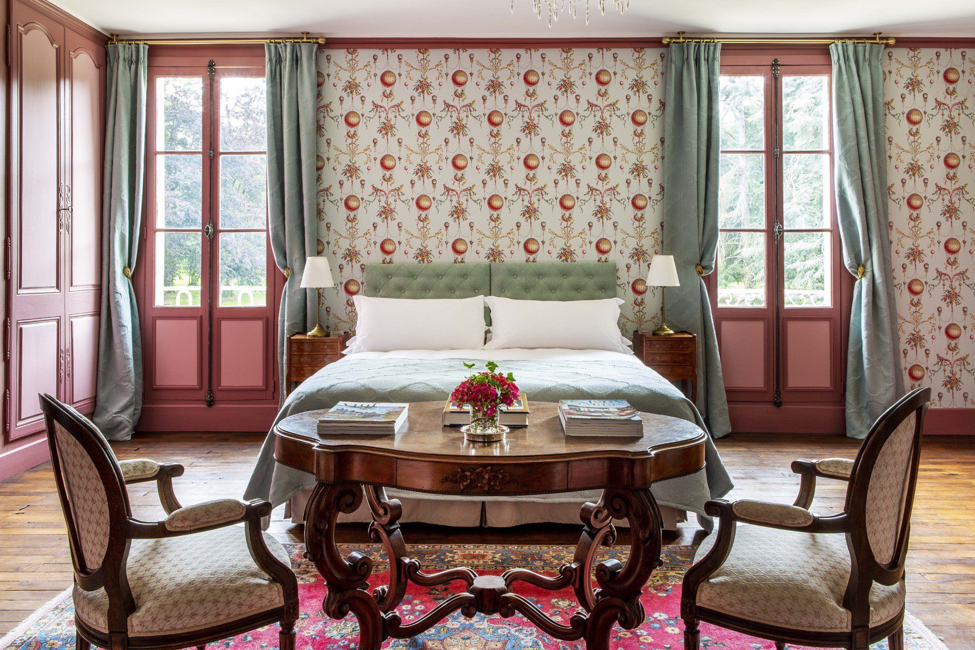 Een slaapkamer met een groot bed, twee nachtkastjes, een ronde tafel met stoelen en behang met een bloemenmotief.