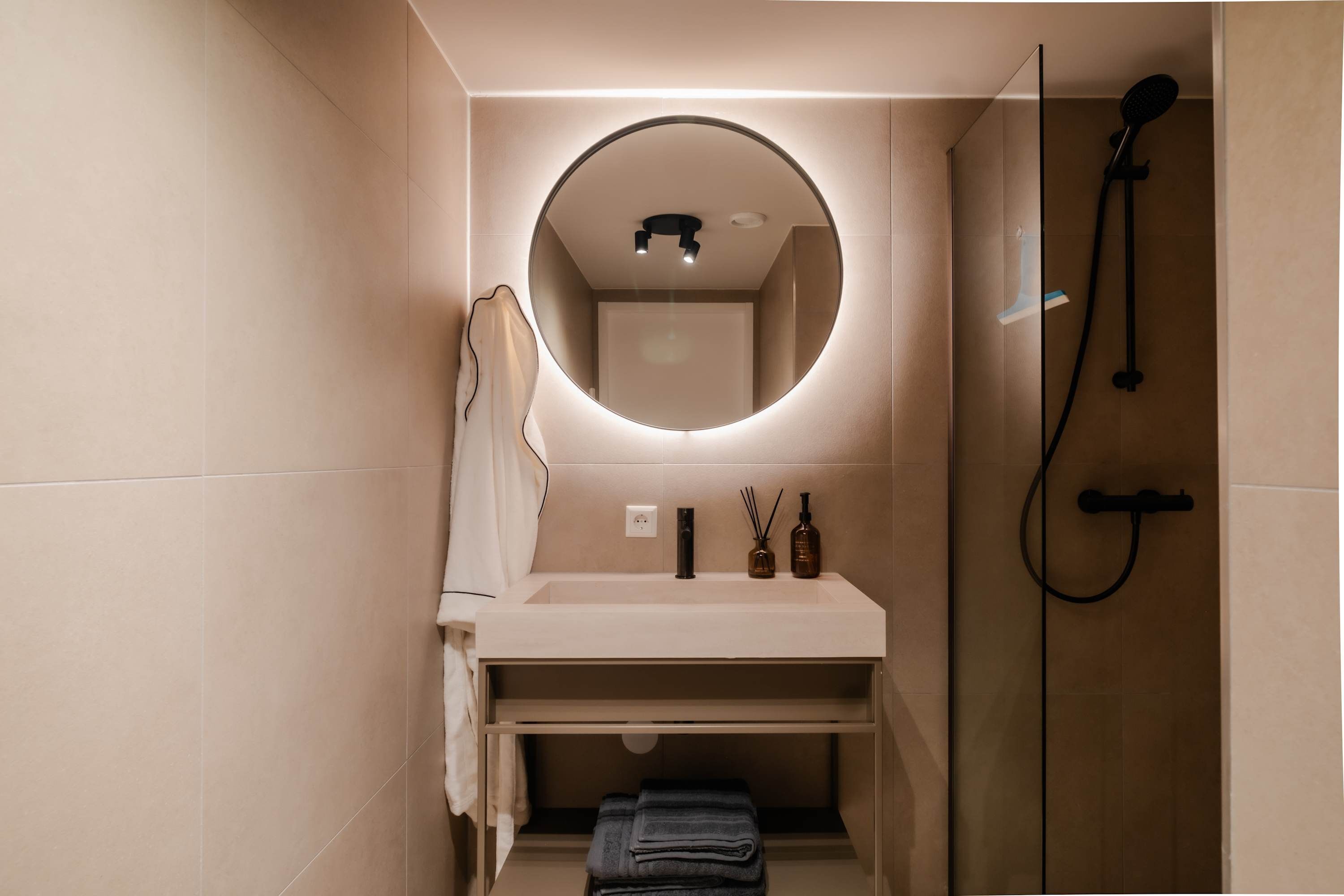A bathroom with a round mirror, a sink, a towel rack, and a shower.