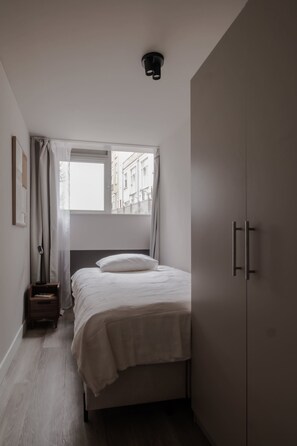 A bedroom with a bed, a wardrobe, a window with curtains, and a floor lamp. - Modern Apt in City Centre 2 With Free Parking (Rotterdam)