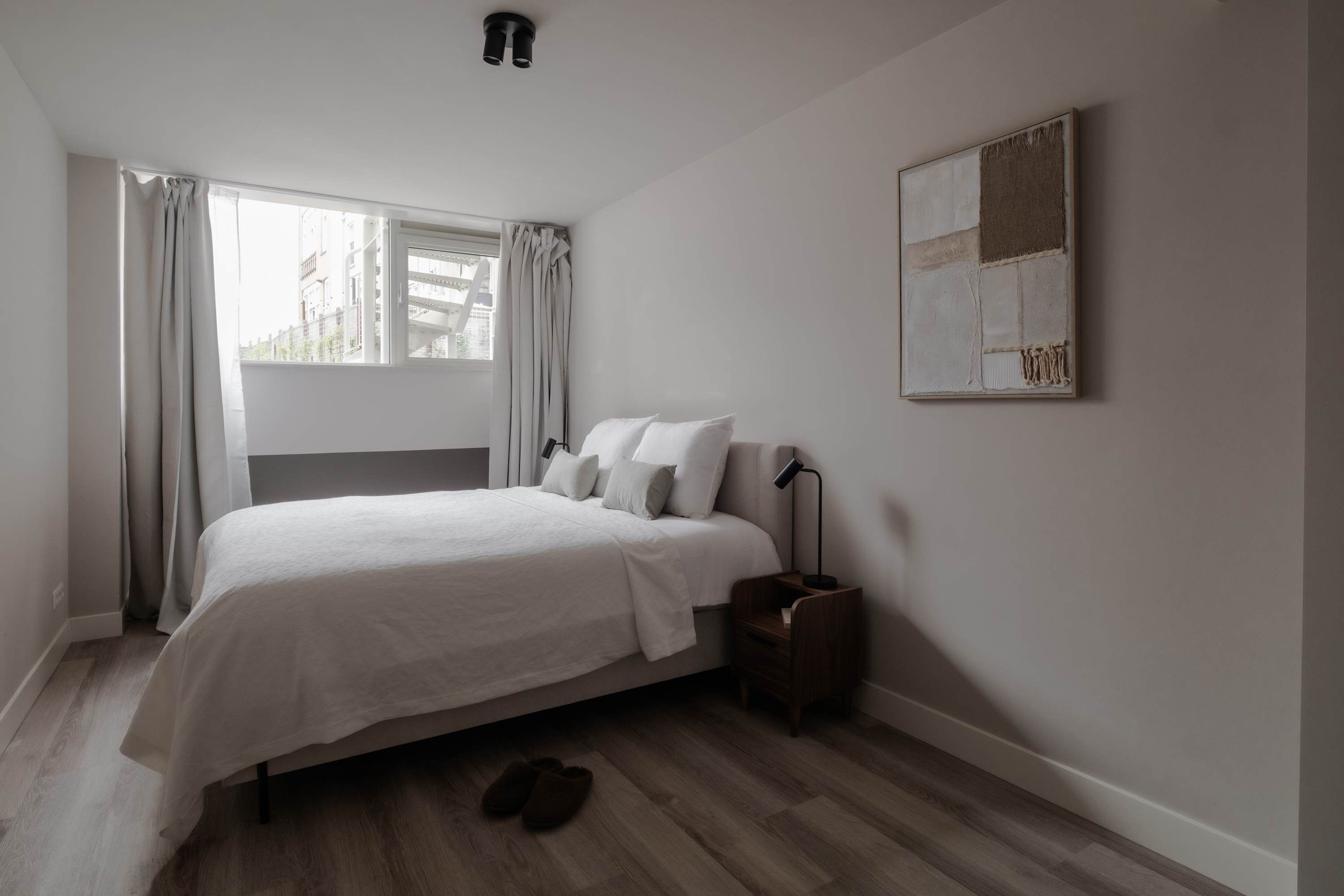 A bedroom with a bed, a nightstand, a lamp, and a window with curtains.