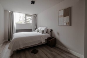 A bedroom with a bed, a nightstand, a lamp, and a window with curtains.