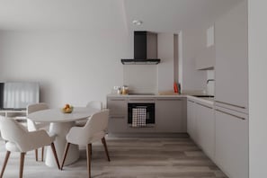 A modern kitchen with a round dining table, white chairs, and a built-in oven.