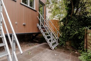 A residential building with a metal staircase leading to a door, a wooden fence, and a garden area with overgrown vegetation. - Spacious 2BR in Heart of Schiedam (Schiedam)