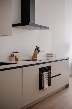 Una cocina moderna con extractor de aire negro, horno empotrado y encimera con un bloque para cuchillos y frascos.